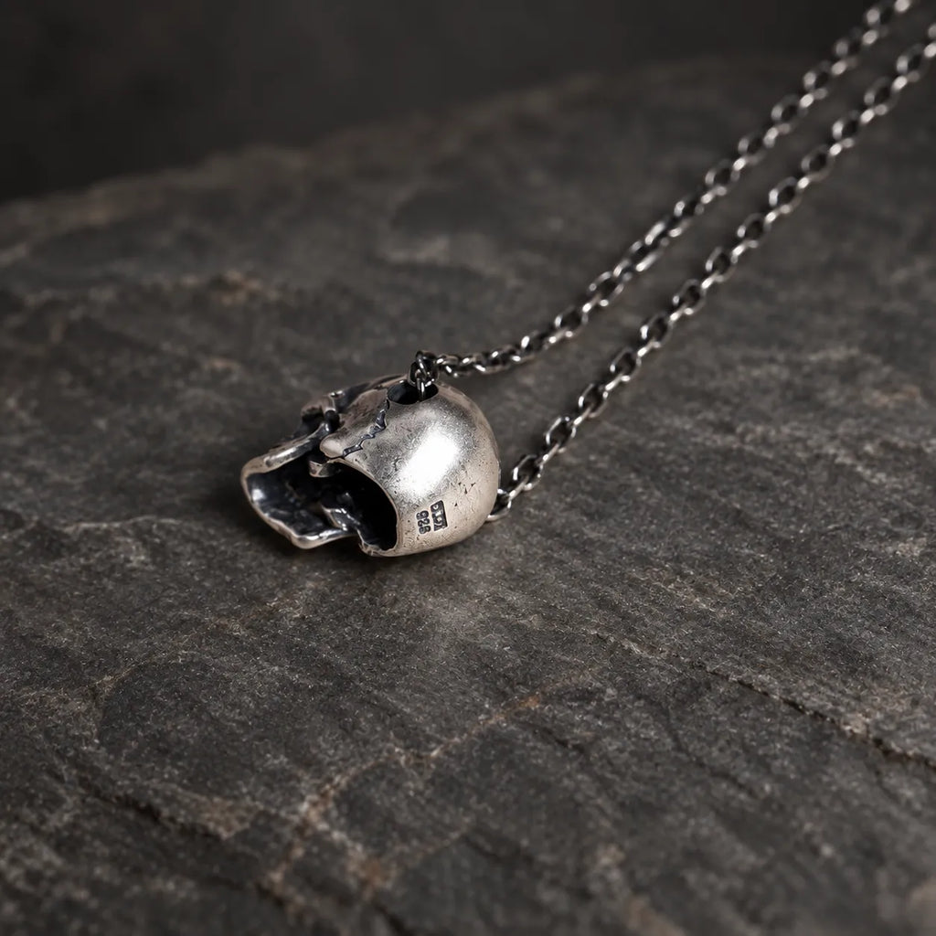Rear view of an oxidized sterling silver articulated skull pendant showing its hollow construction and side-threaded chain