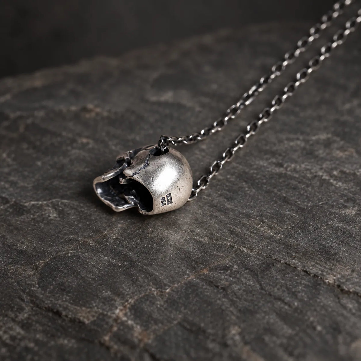 Rear view of an oxidized sterling silver articulated skull pendant showing its hollow construction and side-threaded chain