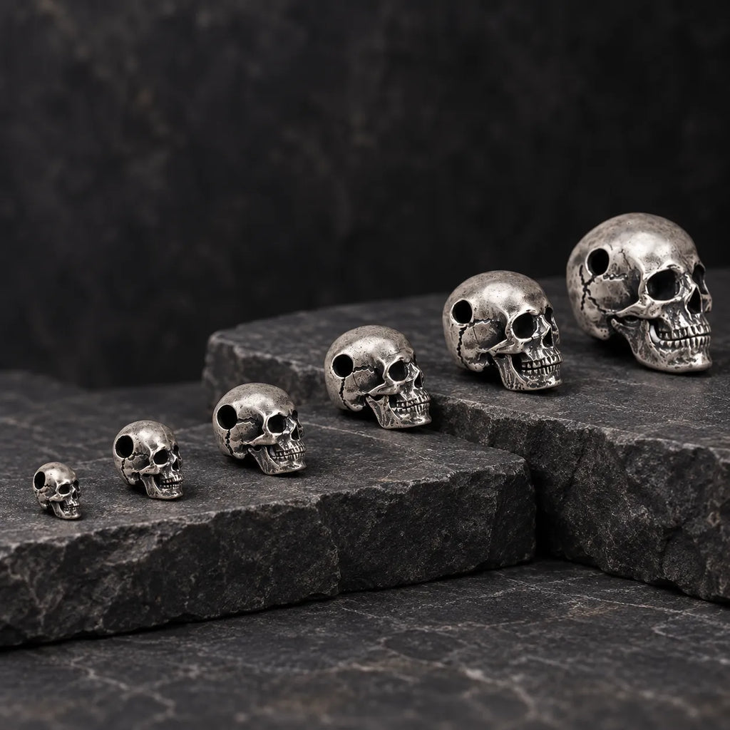 Six graduated sizes of oxidized silver articulated skull pendants displayed across dark stone