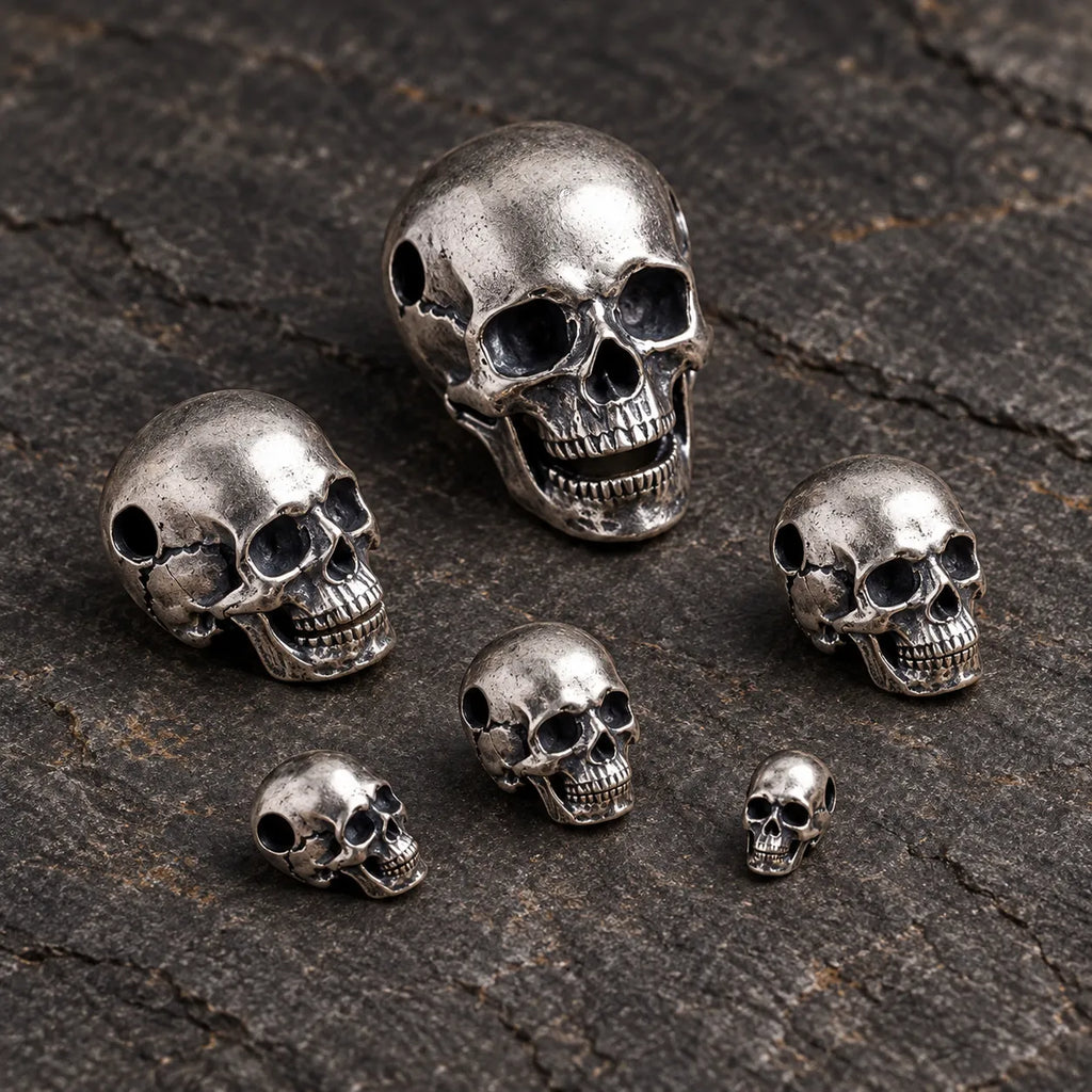 Six sizes of oxidized silver articulated skull pendants arranged in a loose cluster on dark stone