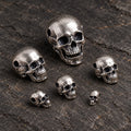 Six sizes of oxidized silver articulated skull pendants arranged in a loose cluster on dark stone