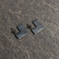 Angled view of open square stud earrings showing their flat surfaces and straight posts