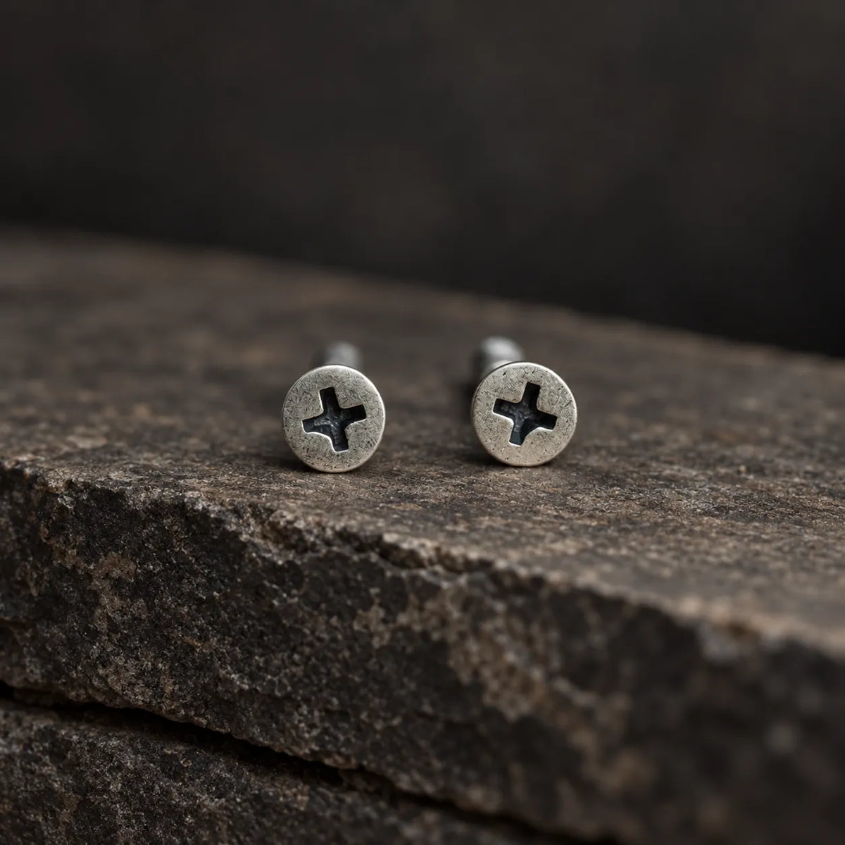 Close front view of round oxidized silver earrings with recessed cross-shaped screw slots