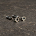 Pair of oxidized sterling silver cross-slot screw stud earrings on dark stone