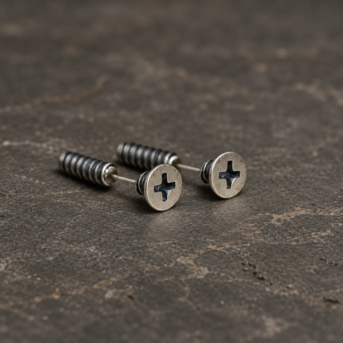 Pair of oxidized sterling silver cross-slot screw stud earrings on dark stone