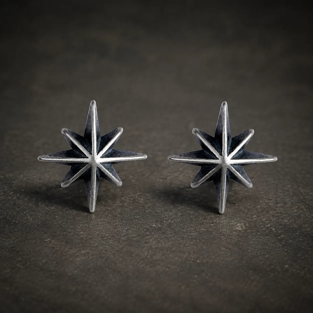 Pair of oxidized 925 sterling silver eight-point starburst stud earrings on a dark stone background