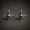 Pair of oxidized 925 sterling silver eight-point starburst stud earrings on a dark stone background