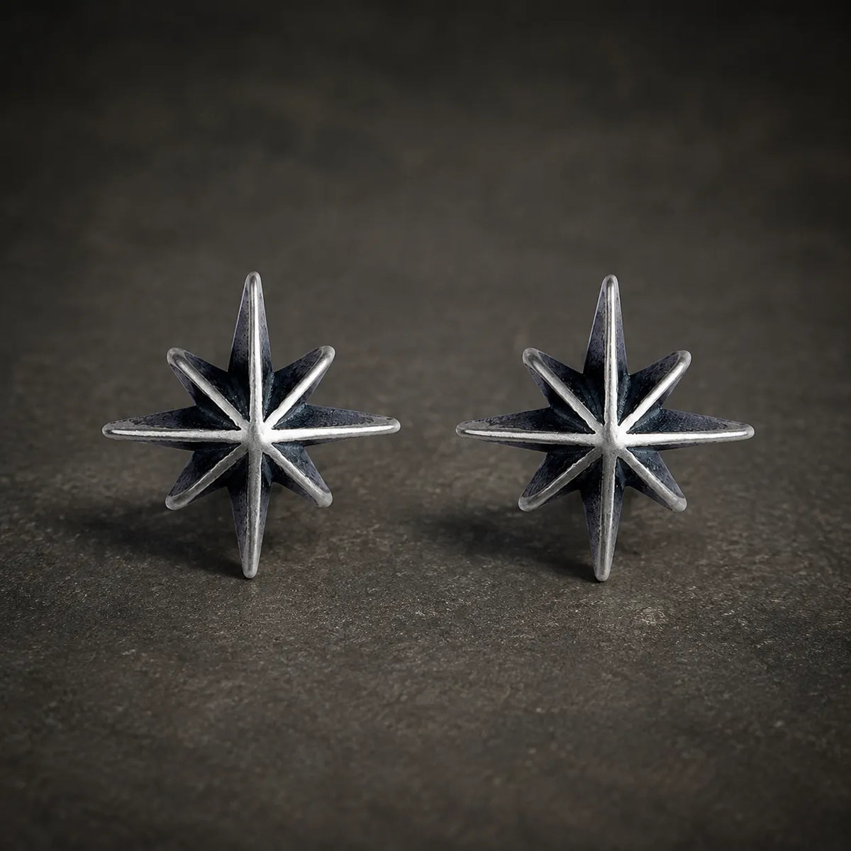 Pair of oxidized 925 sterling silver eight-point starburst stud earrings on a dark stone background