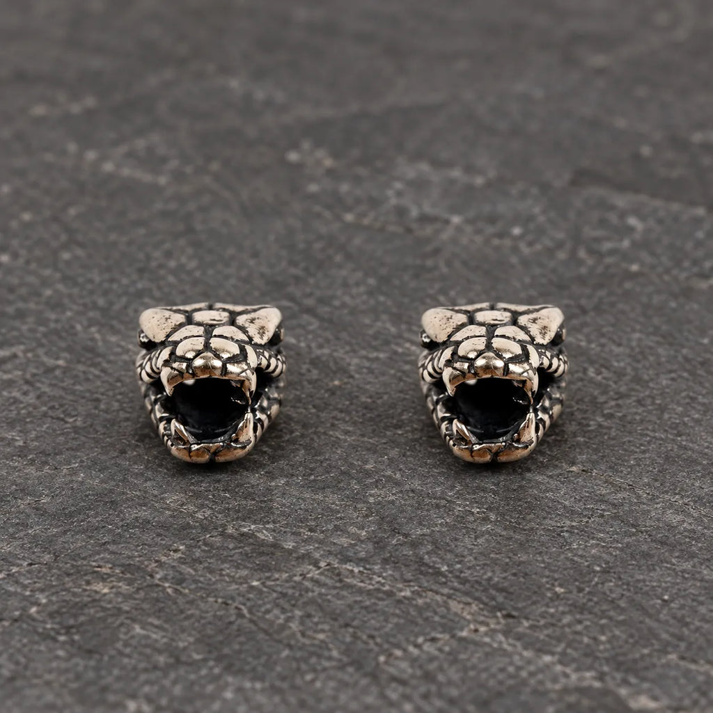 Pair of oxidized 925 sterling silver fanged serpent head stud earrings on dark stone