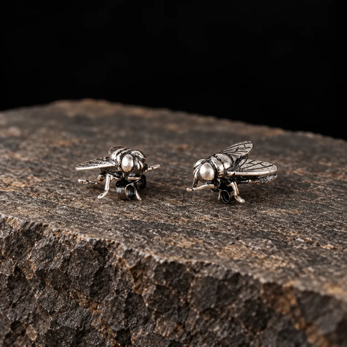 Low side view of oxidized silver fly stud earrings showing their sculptural depth