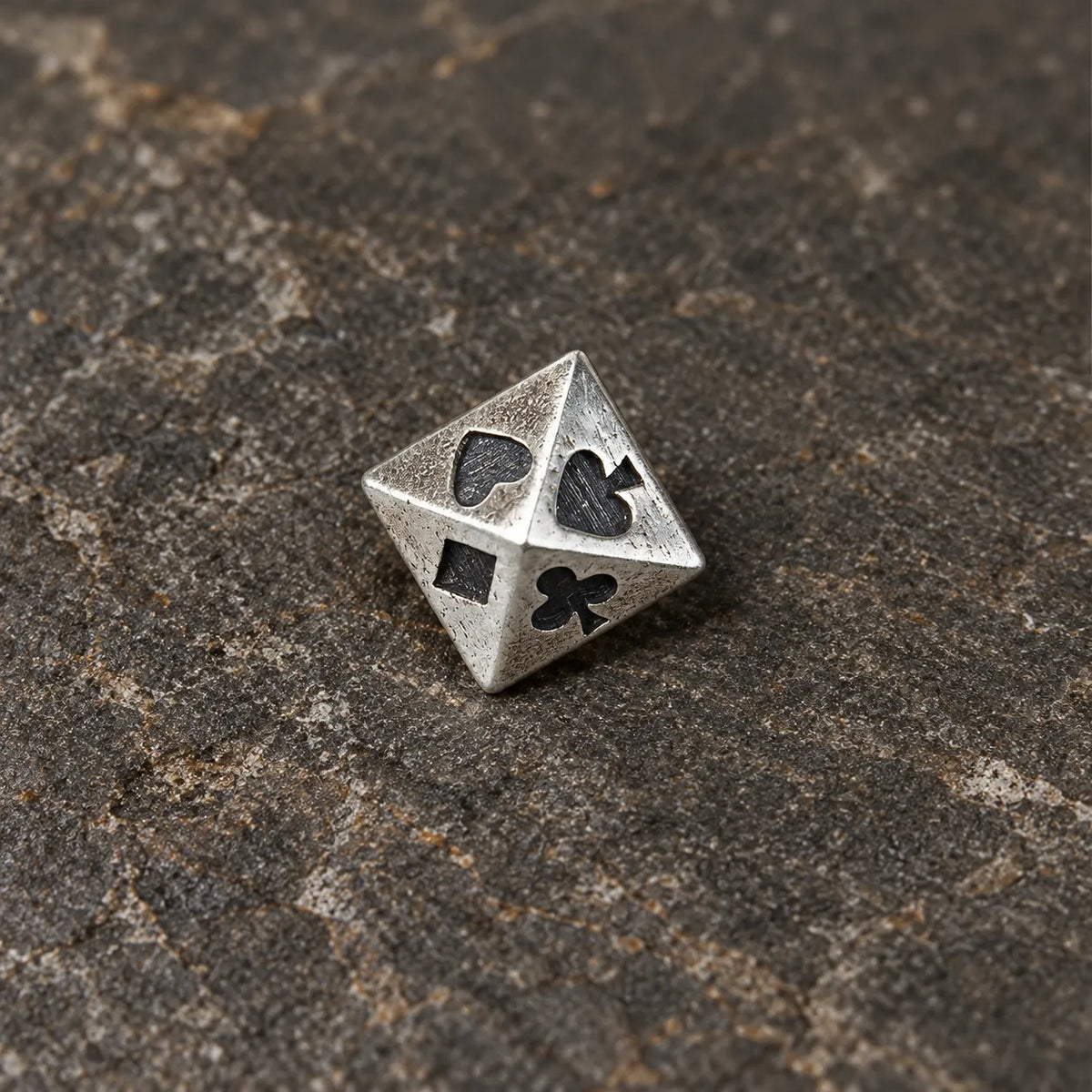 Close-up of a silver pyramid stud engraved with spade heart club and diamond symbols