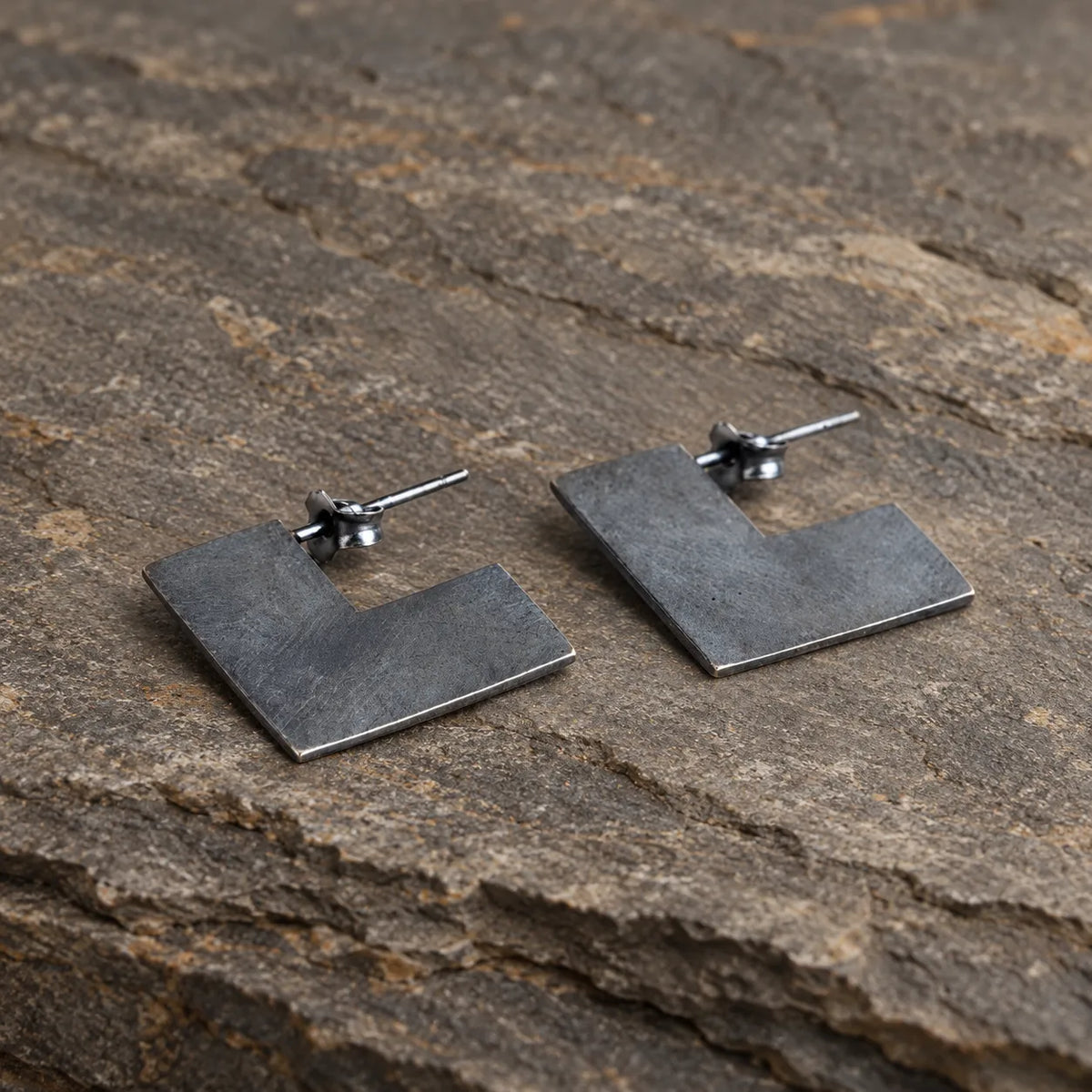 Black oxidized geometric square earrings arranged naturally on gray stone