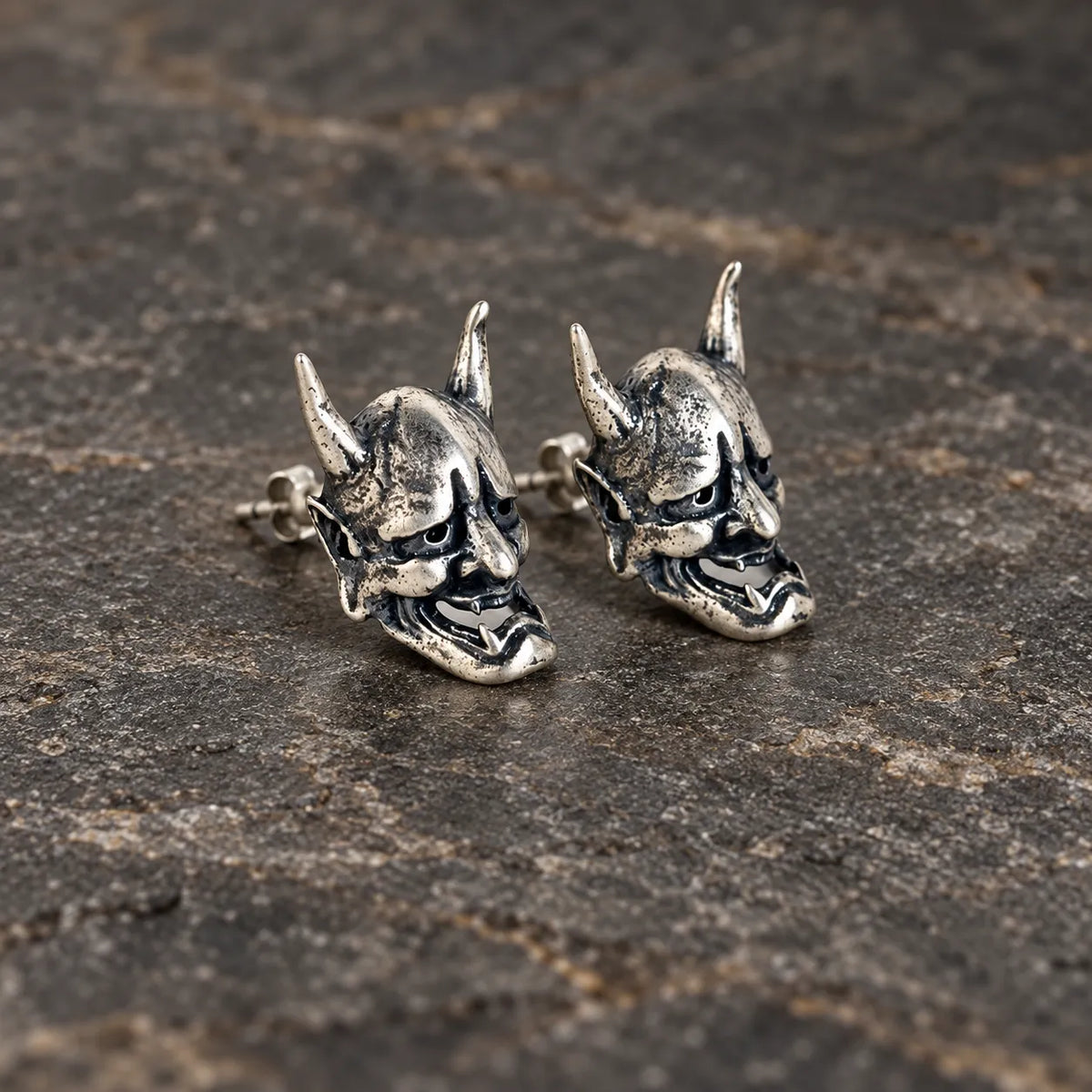 Angled view of oxidized silver Hannya mask stud earrings with visible posts and backs