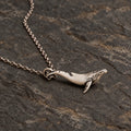 Side view of the sculptural whale pendant resting on dark stone with an optional chain