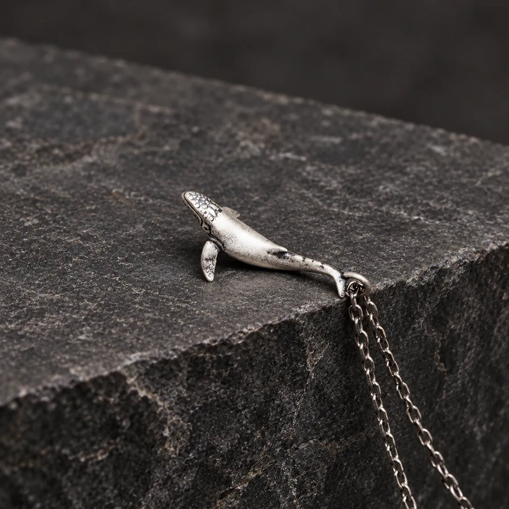 Side profile of an oxidized silver whale pendant showing its curved three-dimensional body