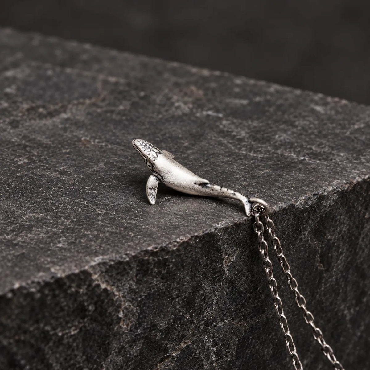 Side profile of an oxidized silver whale pendant showing its curved three-dimensional body