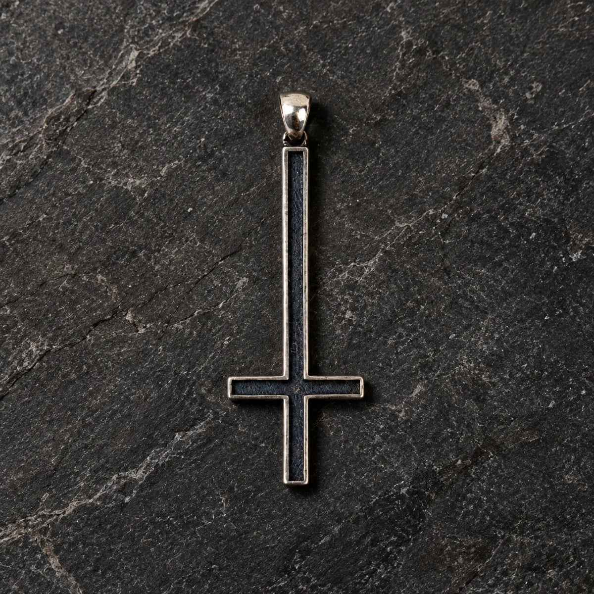 Front view of an oxidized 925 sterling silver inverted cross pendant on dark stone
