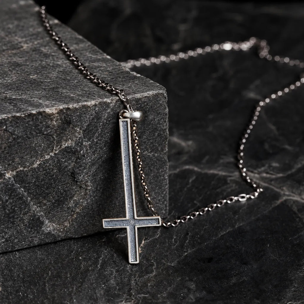 Inverted cross pendant hanging naturally from an optional oxidized silver chain over dark stone