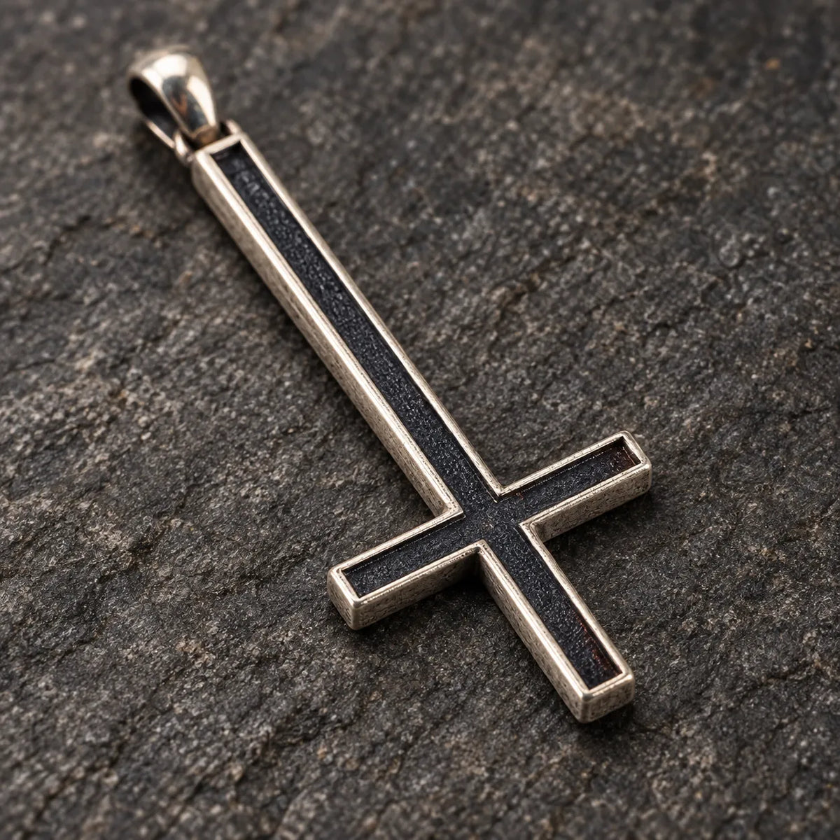 Close-up of the dark oxidized center and raised silver border of an inverted cross pendant