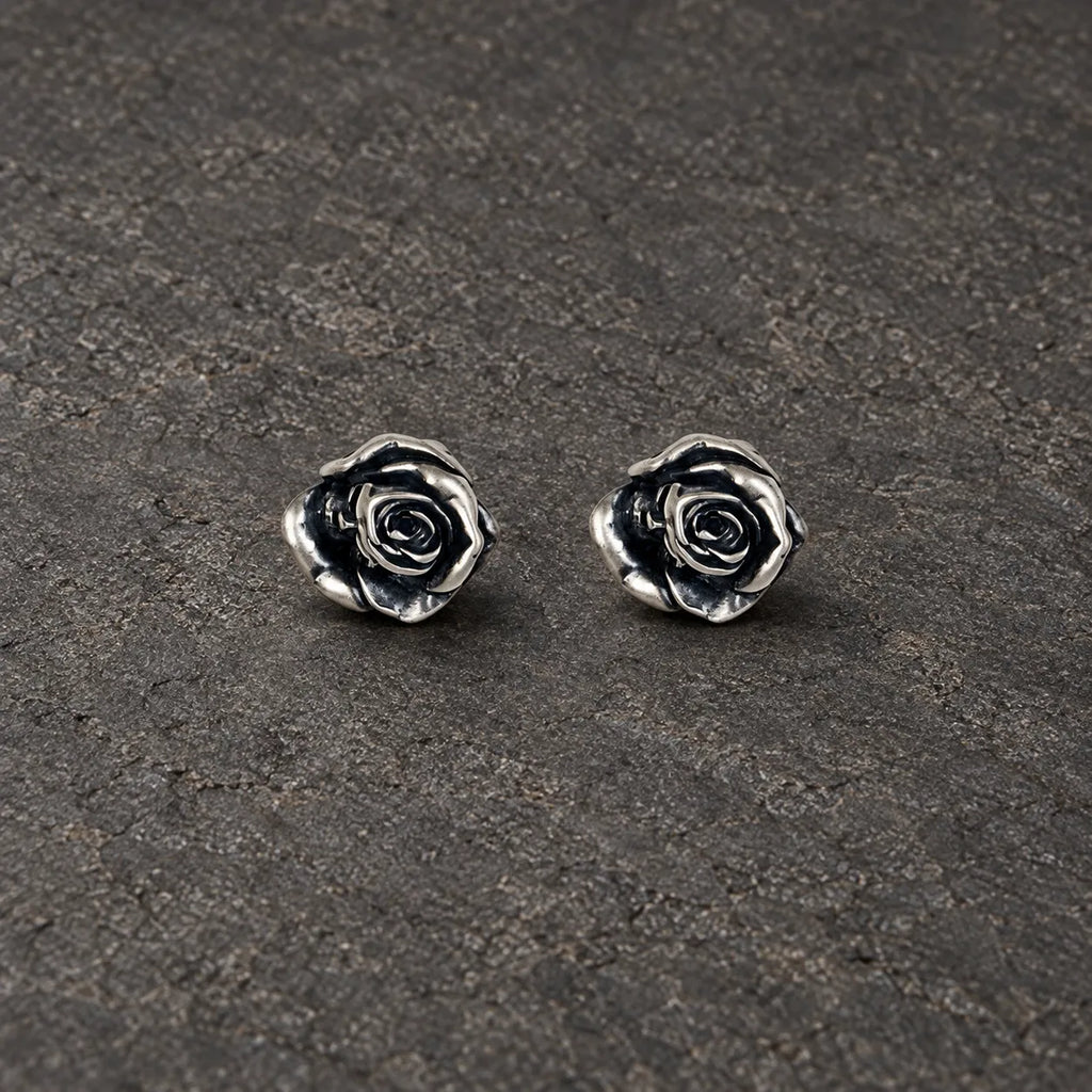 Pair of oxidized sterling silver rose stud earrings on dark stone