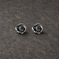 Pair of oxidized sterling silver rose stud earrings on dark stone