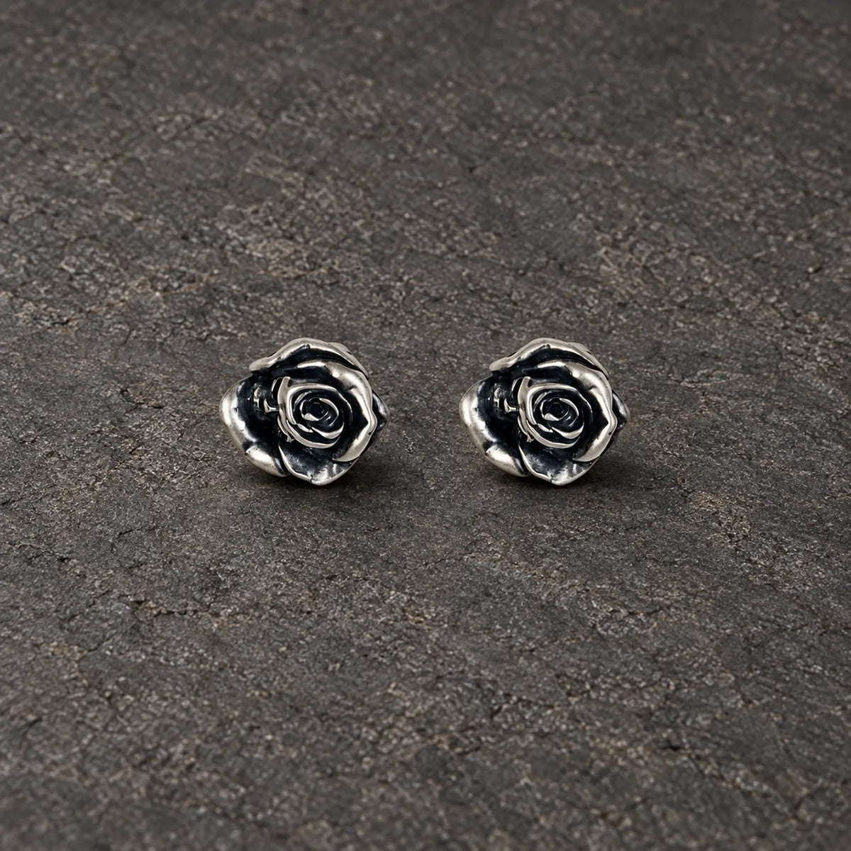 Pair of oxidized sterling silver rose stud earrings on dark stone