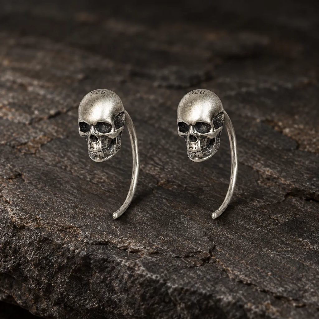 Pair of oxidized 925 sterling silver mini skull hook earrings on dark stone
