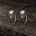 Pair of oxidized 925 sterling silver mini skull hook earrings on dark stone