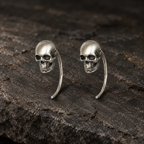 Pair of oxidized 925 sterling silver mini skull hook earrings on dark stone