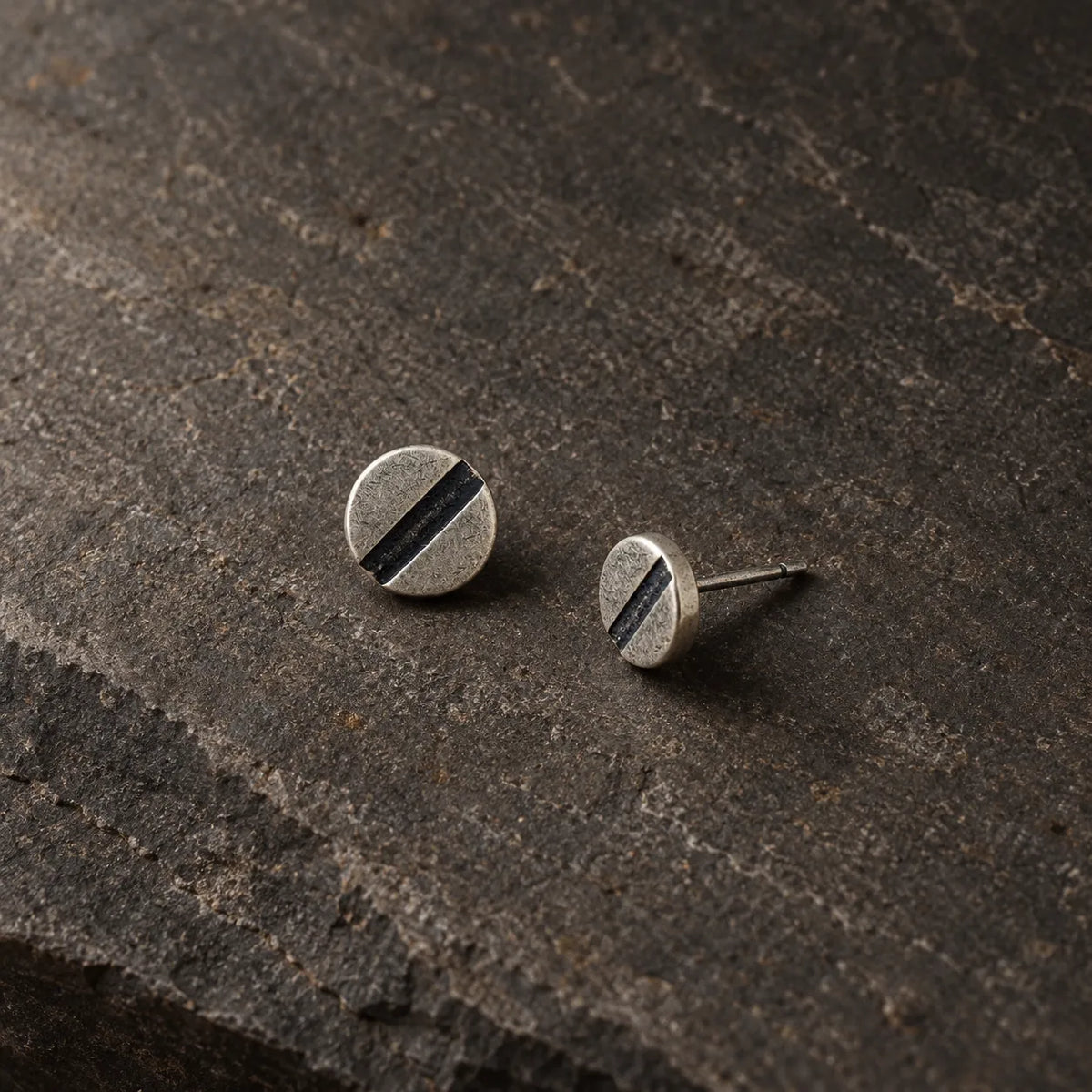 Minimalist silver line disc stud earrings arranged on a charcoal stone surface