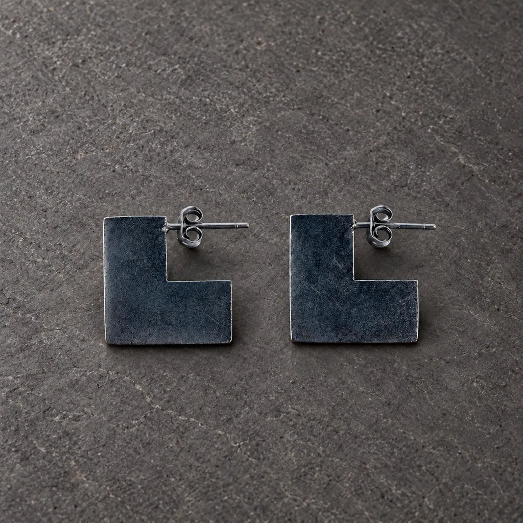 Pair of black oxidized sterling silver broken square stud earrings on gray stone