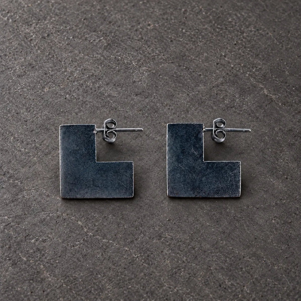 Pair of black oxidized sterling silver broken square stud earrings on gray stone