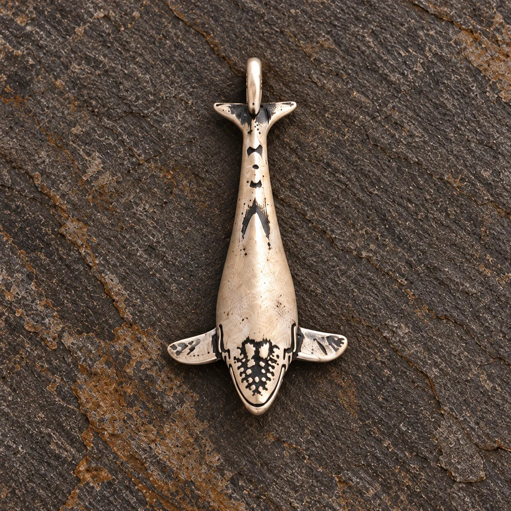 Close view of an oxidized silver humpback whale pendant showing its engraved head and fins
