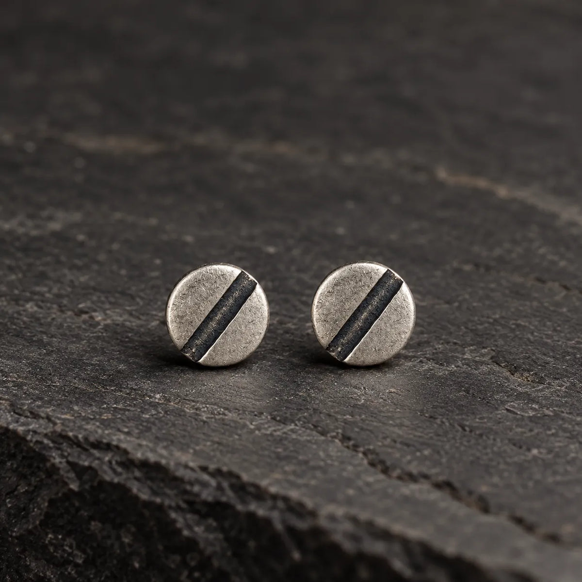 Pair of oxidized 925 sterling silver line disc stud earrings on dark stone