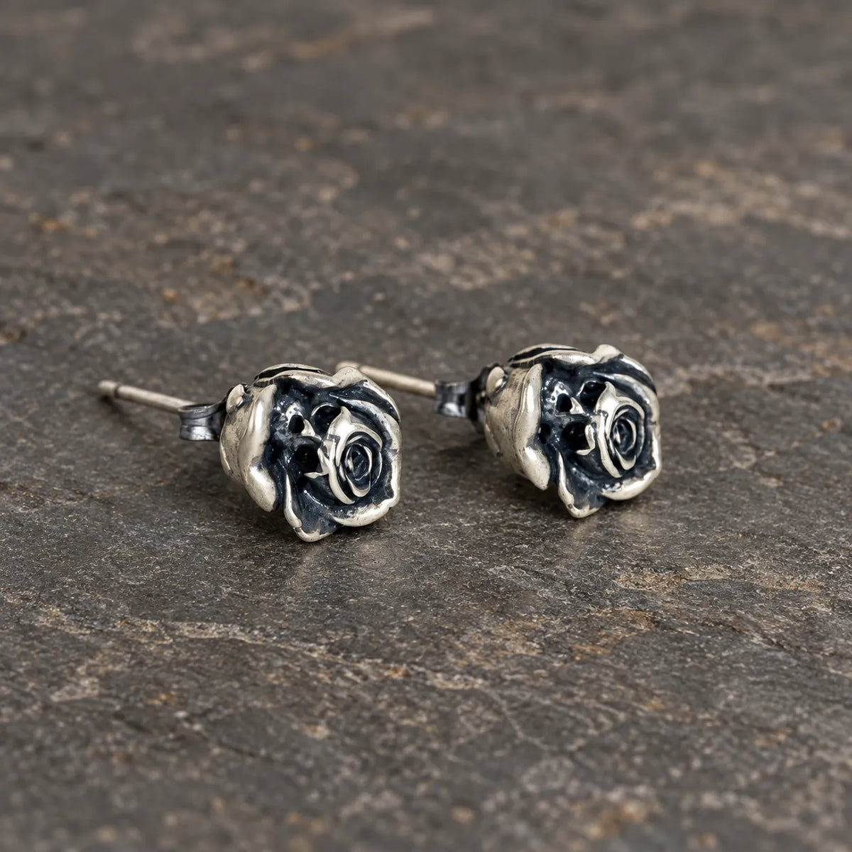 Angled view of sculpted rose stud earrings showing their posts and butterfly backs