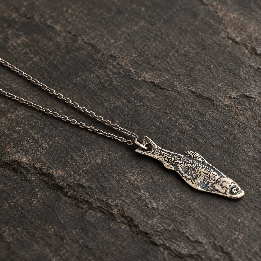 Angled view of an oxidized silver fishbone pendant showing its engraved skeletal pattern