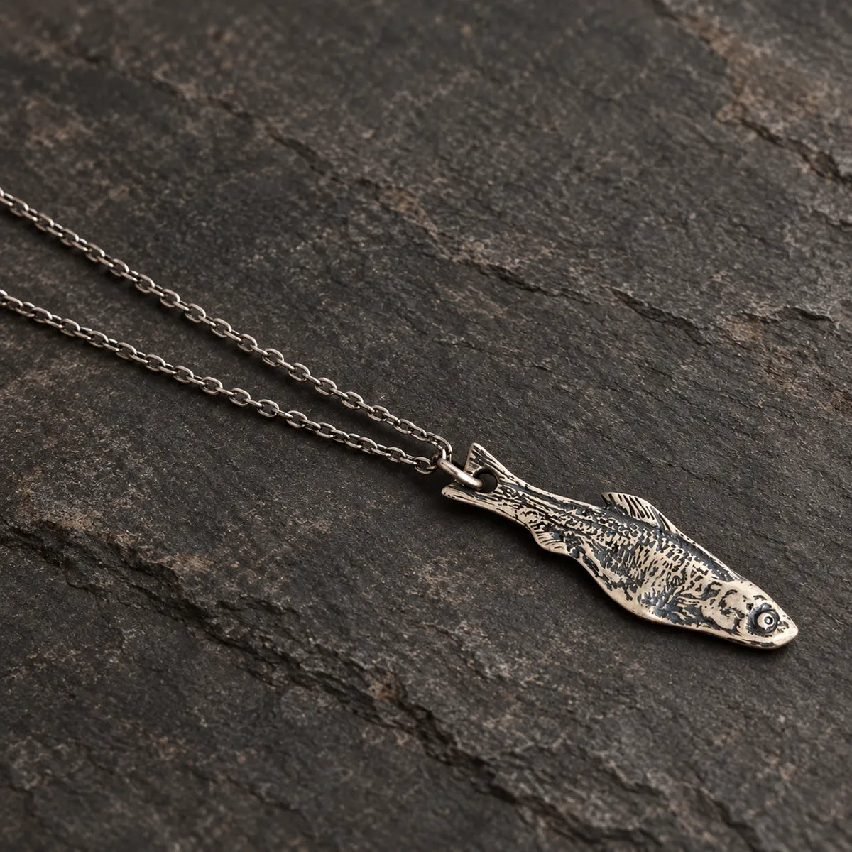 Angled view of an oxidized silver fishbone pendant showing its engraved skeletal pattern