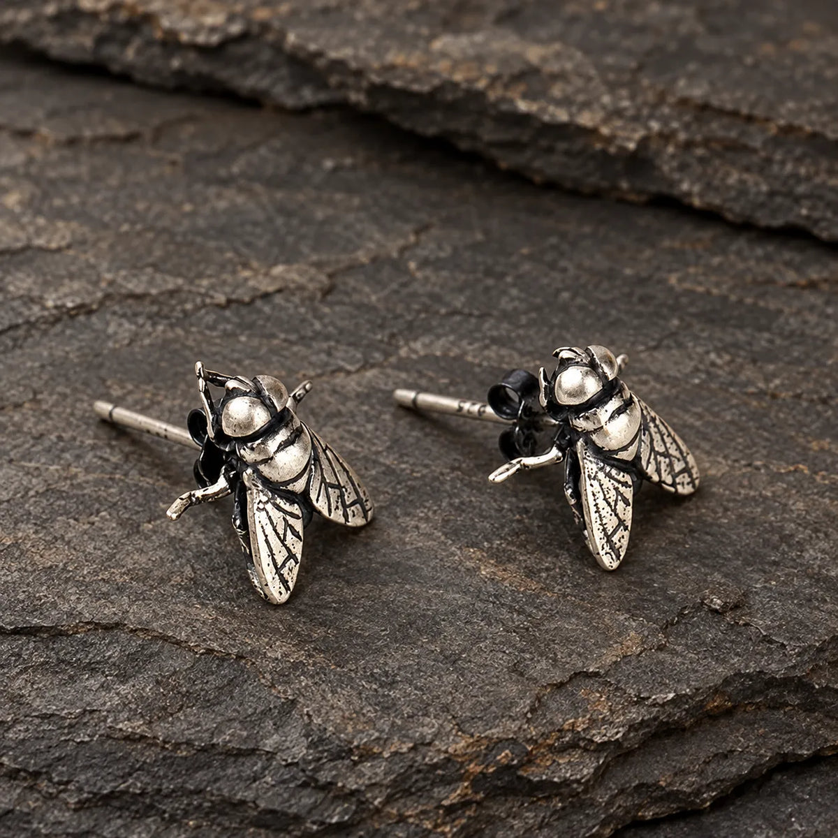 Close view of silver fly earrings showing engraved wing veins and segmented bodies