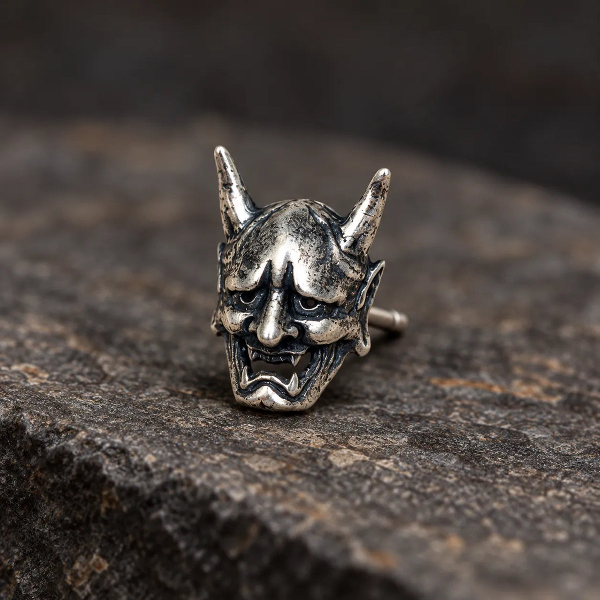 Close view of an oxidized silver Hannya mask stud showing its horns, fangs and sculpted expression