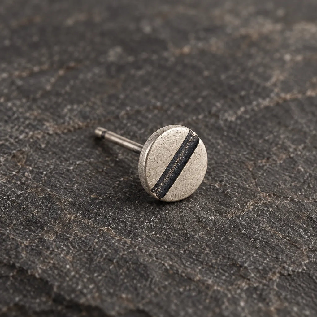 Close-up of a matte silver disc stud with a single dark oxidized recessed line