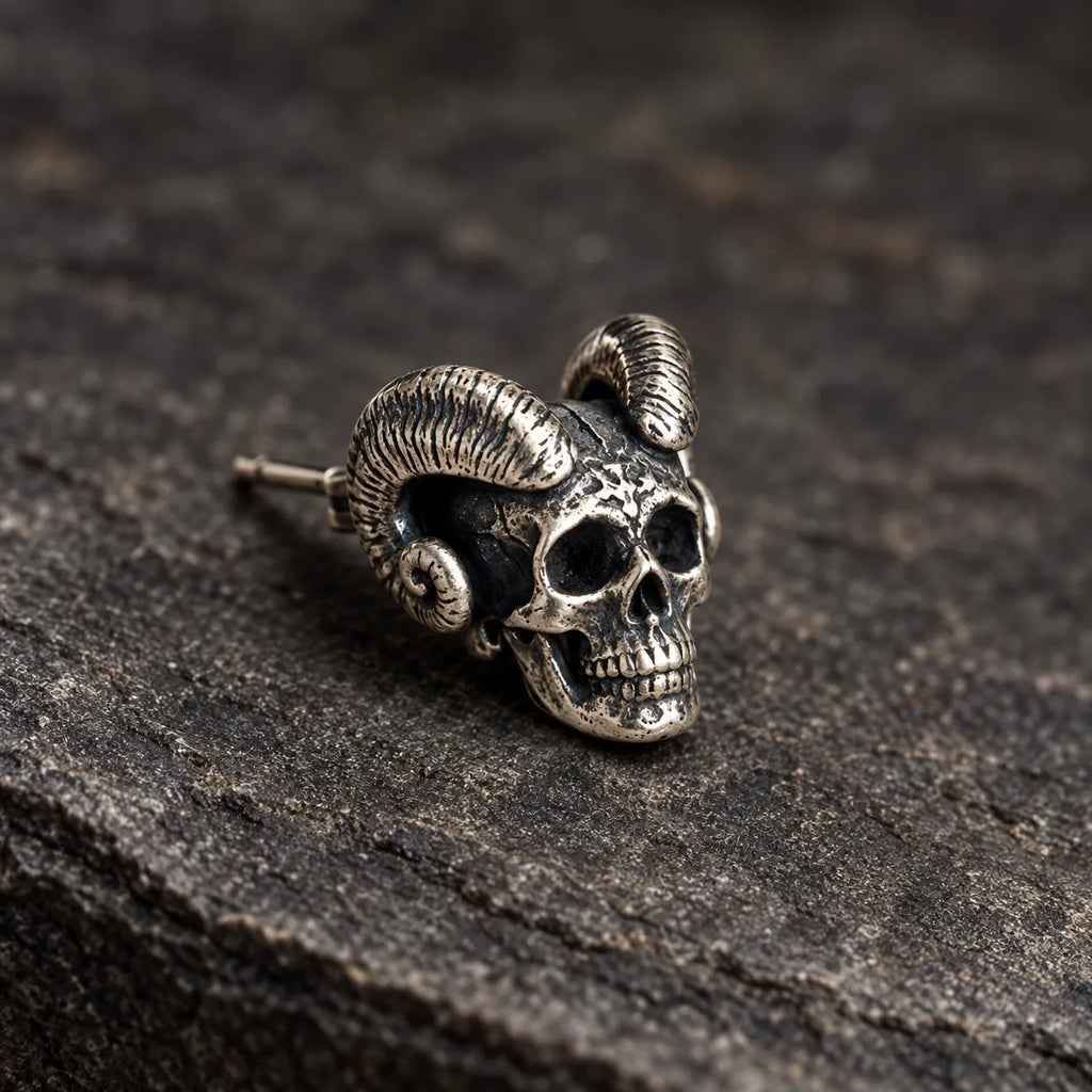 Close-up of an oxidized silver skull stud showing its curled horns, dark eye sockets and carved teeth