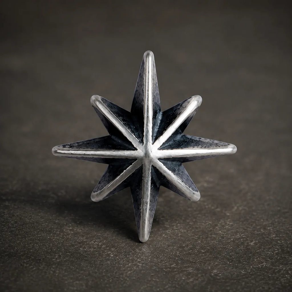 Close-up of an oxidized silver eight-point starburst stud with polished ridges and dark recessed details