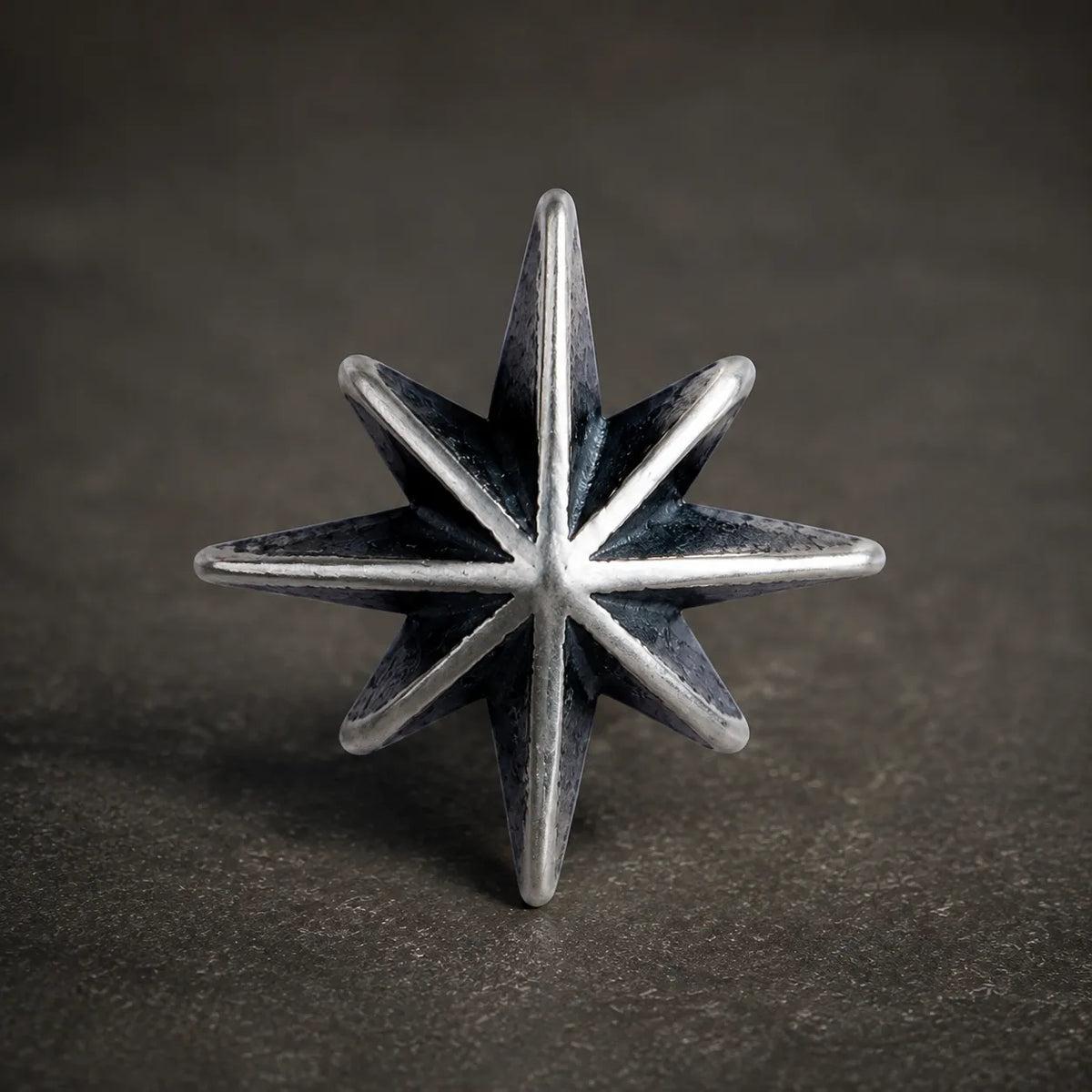 Close-up of an oxidized silver eight-point starburst stud with polished ridges and dark recessed details