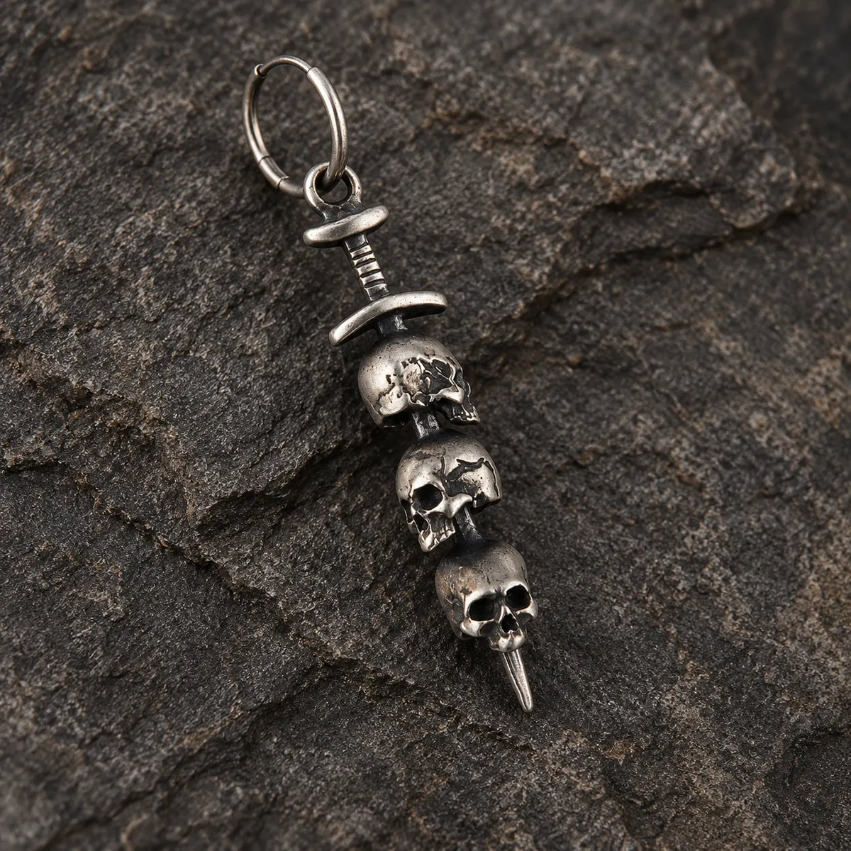 Close-up of an oxidized silver sword earring with three stacked skulls and a pointed blade