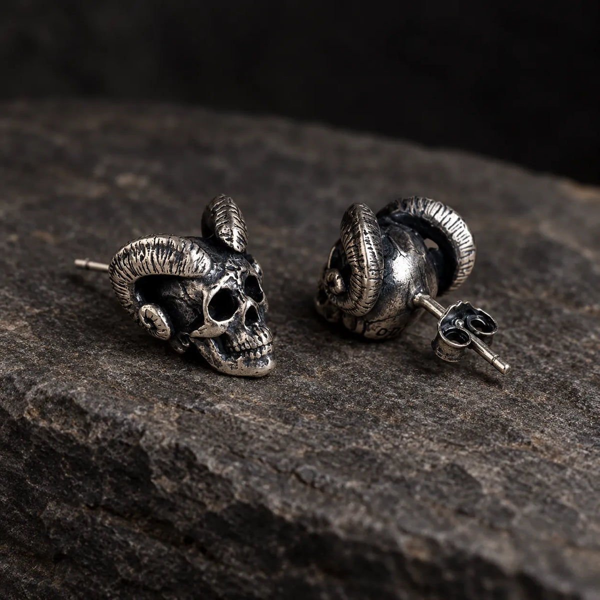 Angled view of ram-horn skull earrings showing their straight posts and butterfly backs