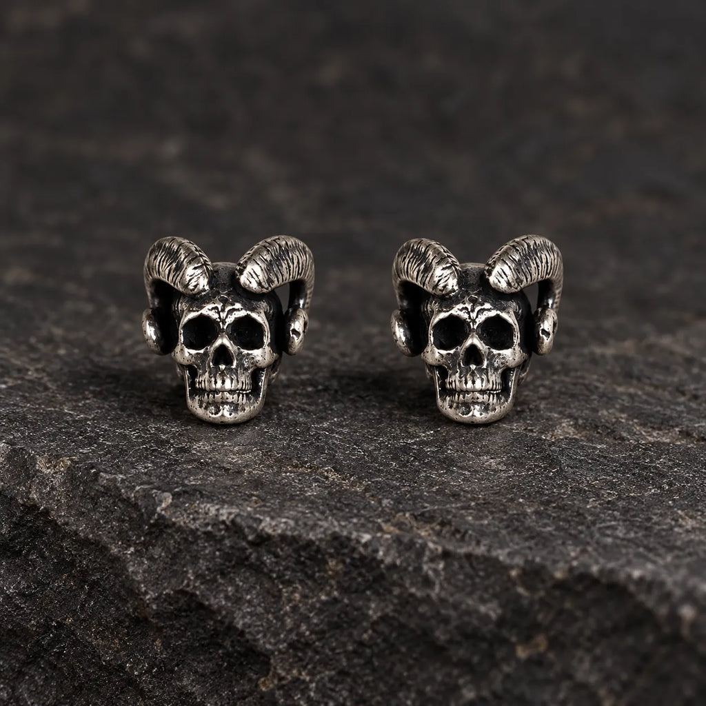 Pair of oxidized 925 sterling silver ram-horn skull stud earrings on dark stone