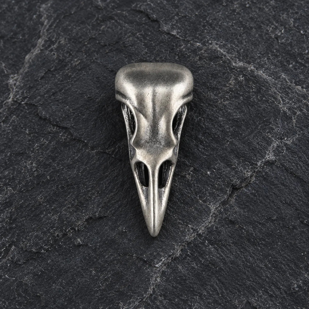 Front view of an oxidized 925 sterling silver raven skull pendant on dark stone