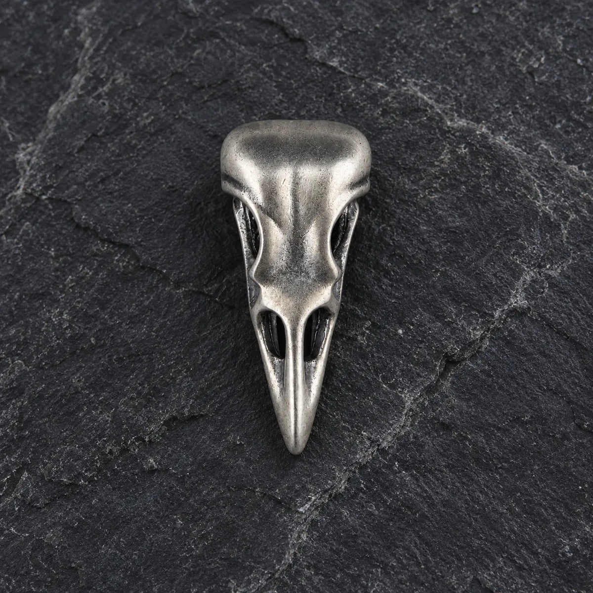 Front view of an oxidized 925 sterling silver raven skull pendant on dark stone