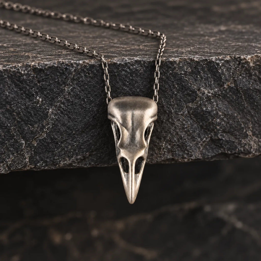 Raven skull pendant hanging naturally from an optional 2.0 mm chain over dark stone