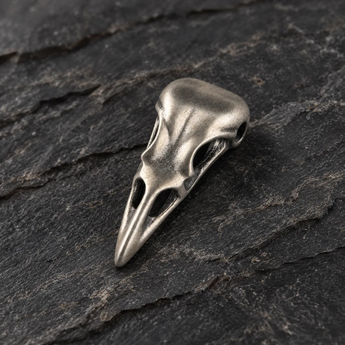 Three-quarter view of an oxidized silver raven skull pendant showing its sculptural depth